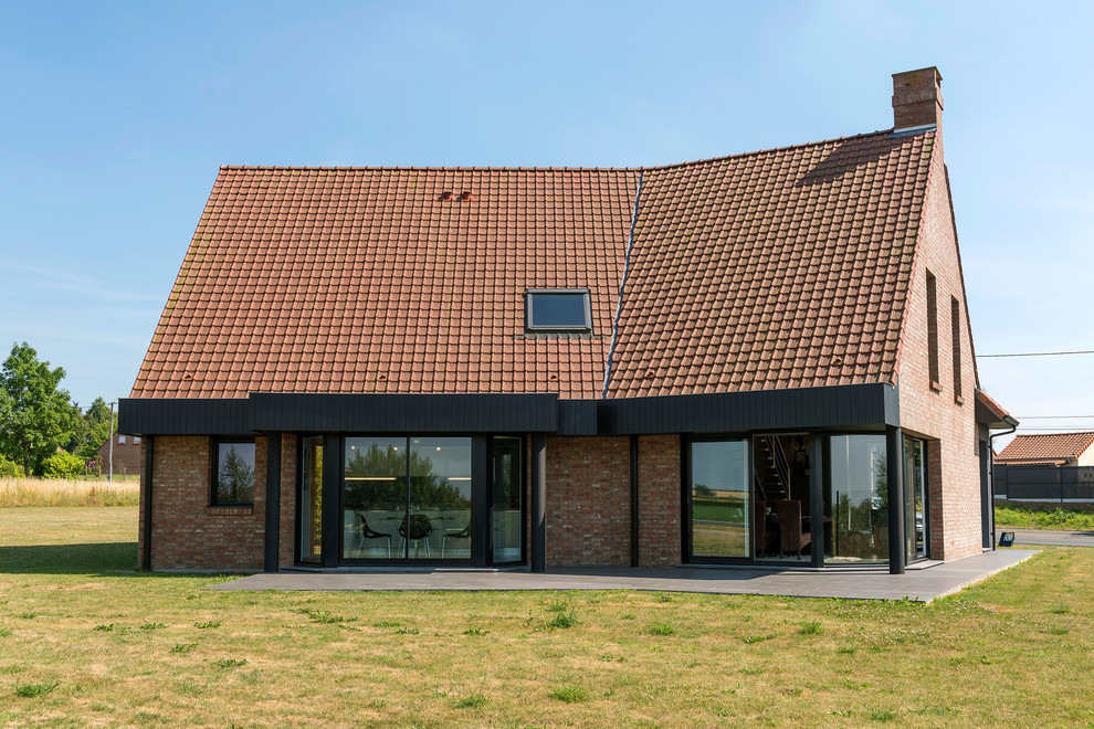 Aménagement d'une grande façade de maison rouge contemporaine en brique à un étage avec un toit à deux pans et un toit en tuile.