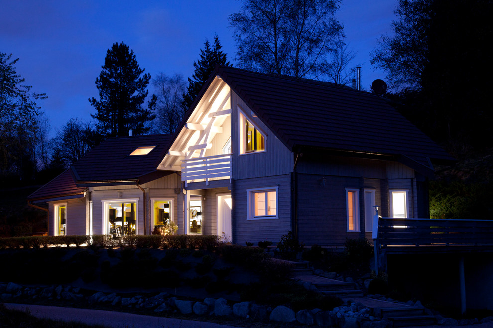 Cette image montre une grande façade de maison grise nordique en bois à niveaux décalés avec un toit à deux pans.