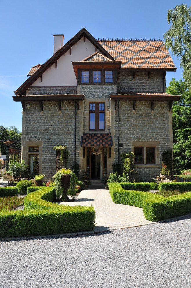 Foto della facciata di una casa classica a tre piani con rivestimento in pietra e tetto a capanna