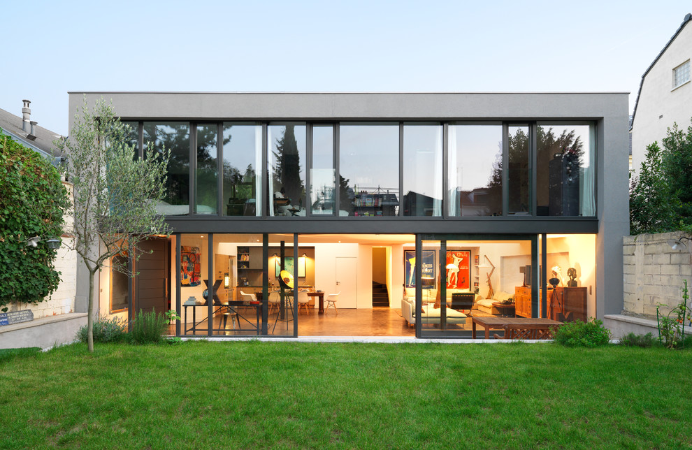 Immagine della facciata di una casa a schiera grande grigia moderna a due piani con rivestimento in vetro, tetto piano e copertura in metallo o lamiera