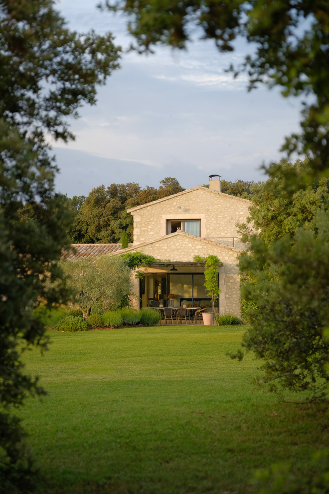 Imagen de fachada de casa beige mediterránea de dos plantas con revestimiento de piedra, tejado a dos aguas y tejado de teja de barro