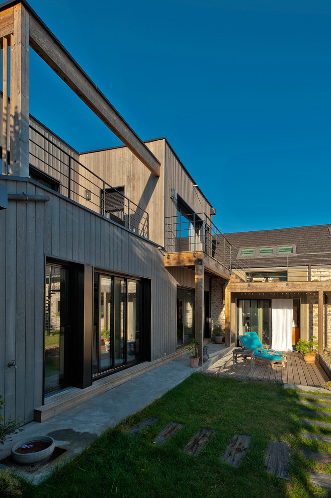 Cette image montre une grande façade de maison design en bois à un étage avec un toit plat et un toit mixte.