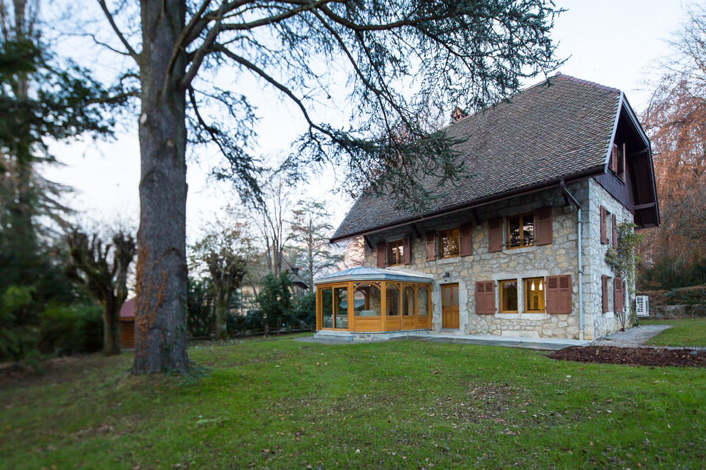На фото: трехэтажный, серый дом среднего размера в стиле кантри с облицовкой из камня и полувальмовой крышей с
