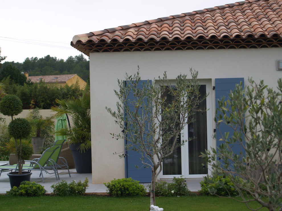 Aménagement d'une grande façade de maison beige méditerranéenne en béton de plain-pied avec un toit à quatre pans et un toit en tuile.