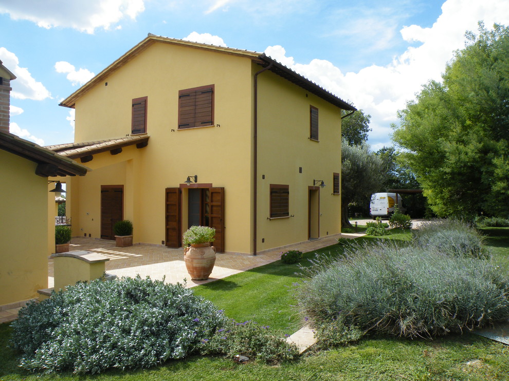 Example of a large cottage yellow two-story stucco house exterior design in Rome with a gambrel roof and a tile roof