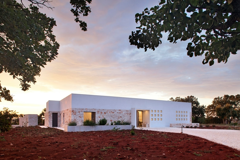 На фото: одноэтажный, белый частный загородный дом среднего размера в стиле кантри с облицовкой из камня и плоской крышей