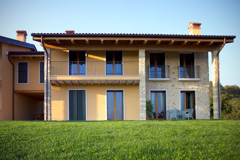 Modelo de fachada de casa bifamiliar amarilla de estilo de casa de campo de dos plantas con revestimientos combinados, tejado a doble faldón y tejado de teja de barro