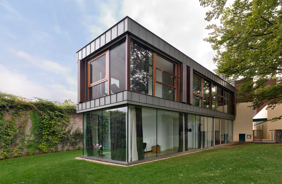 Cette image montre une façade de maison grise design en verre à un étage avec un toit plat.