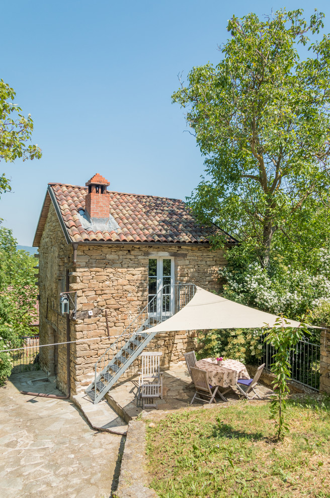 Ejemplo de fachada de casa marrón de estilo de casa de campo pequeña de dos plantas con revestimiento de piedra, tejado a dos aguas y tejado de teja de barro