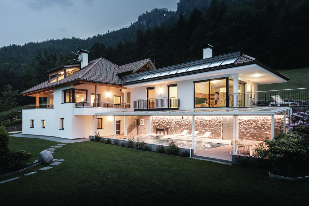 Стильный дизайн: двухэтажный, белый частный загородный дом в современном стиле с комбинированной облицовкой, вальмовой крышей и черепичной крышей - последний тренд