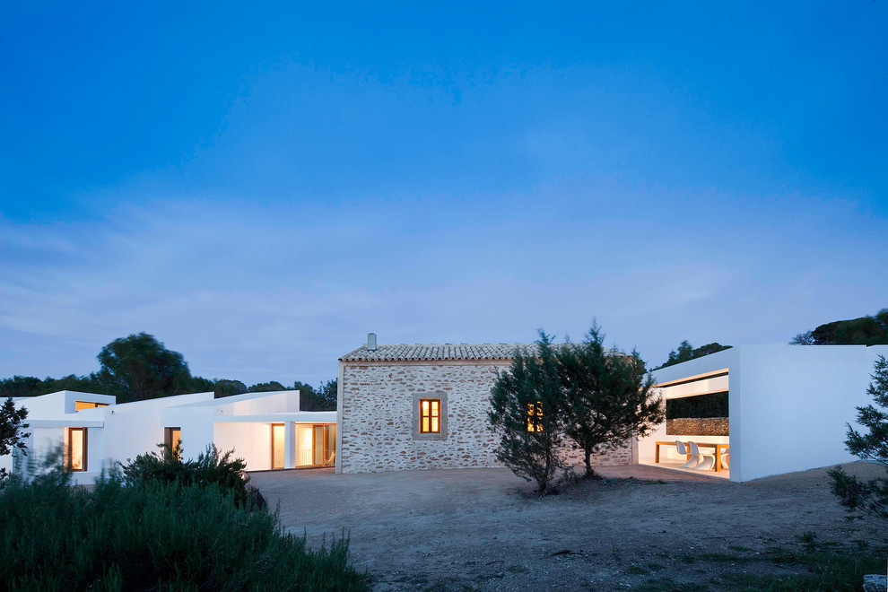 На фото: огромный, белый дом в средиземноморском стиле с разными уровнями, облицовкой из камня и плоской крышей с