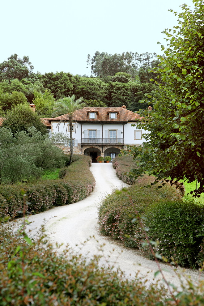 Modelo de fachada blanca campestre de tamaño medio de tres plantas con revestimientos combinados y tejado a cuatro aguas