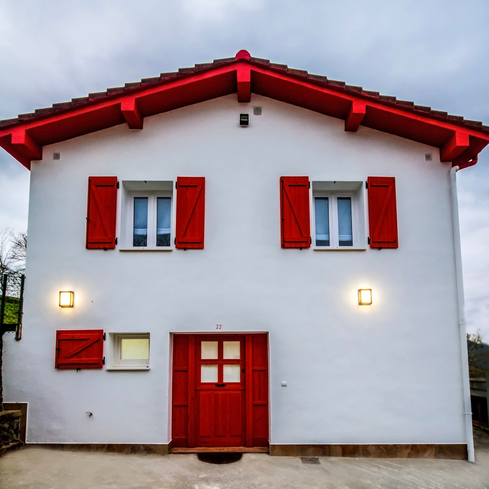 Cette image montre une façade de maison basque blanche rustique de taille moyenne et à un étage avec un revêtement mixte et un toit à deux pans.