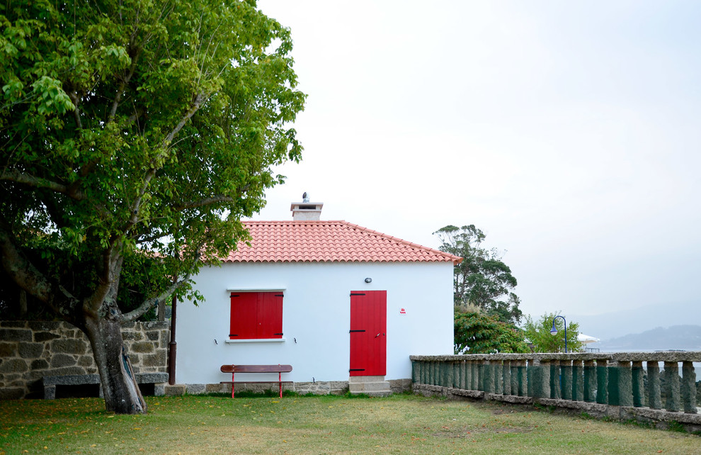 Imagen de fachada de casa blanca marinera pequeña de dos plantas con revestimiento de piedra, tejado a dos aguas y tejado de teja de barro