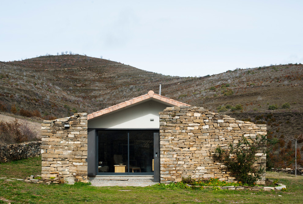 Esempio della facciata di una casa piccola marrone mediterranea a un piano con rivestimento in pietra e tetto a capanna