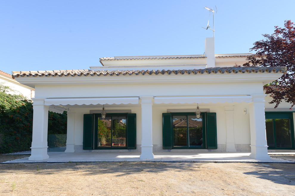 Imagen de fachada blanca mediterránea de tamaño medio de dos plantas con revestimiento de aglomerado de cemento y tejado a cuatro aguas