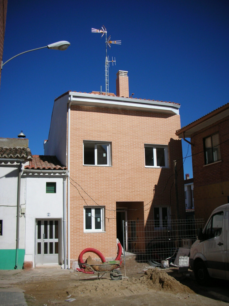 Ejemplo de fachada de piso roja moderna pequeña de tres plantas con revestimiento de ladrillo, tejado a dos aguas y tejado de teja de barro