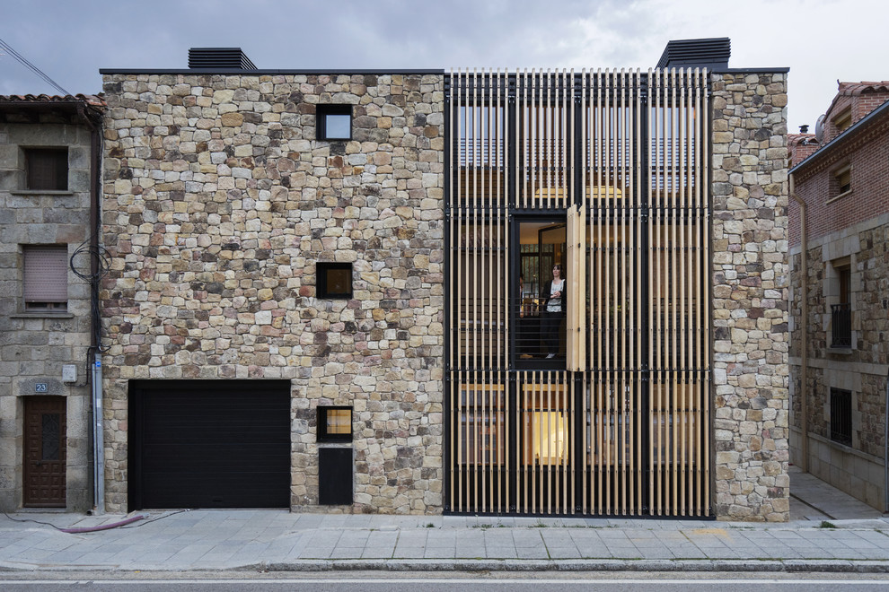 Medium sized and brown contemporary terraced house in Madrid with three floors, stone cladding and a flat roof.