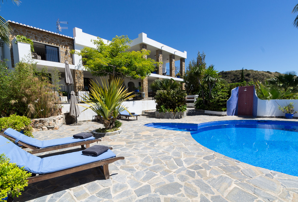 This is an example of a large and white mediterranean two floor detached house in Other with stone cladding, a flat roof and a tiled roof.