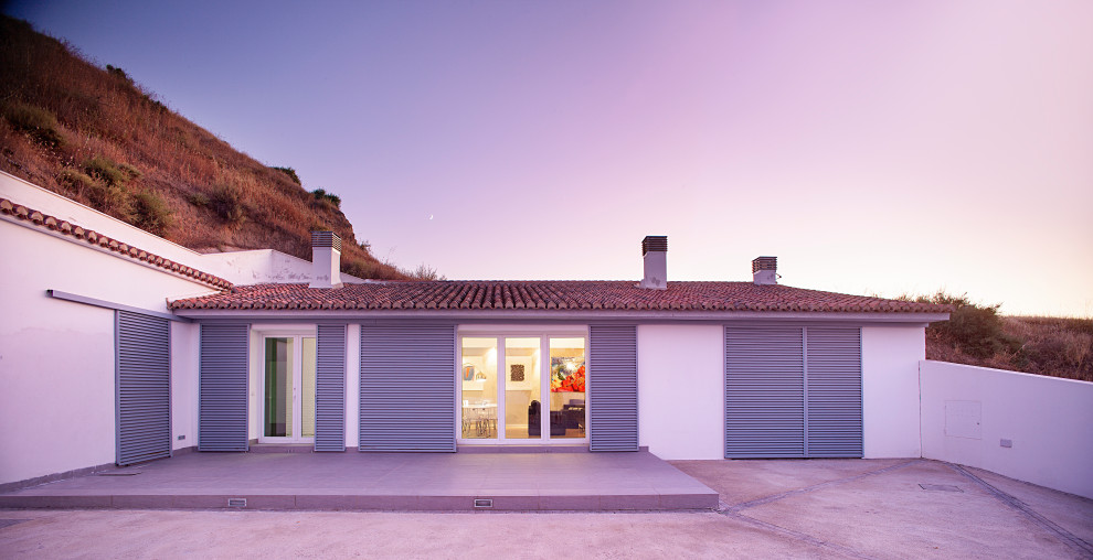 Cette photo montre une façade de maison blanche tendance en béton de taille moyenne et de plain-pied avec un toit en appentis et un toit en tuile.