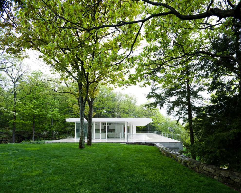Cette image montre une façade de maison blanche minimaliste en verre de taille moyenne et à un étage avec un toit plat.
