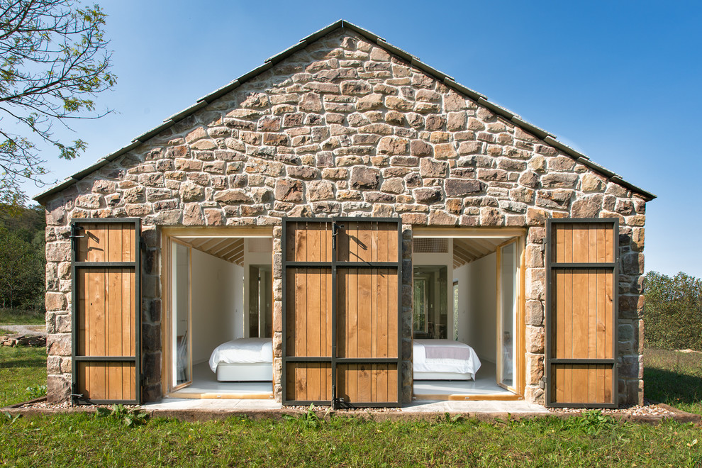Modelo de fachada de casa beige campestre de tamaño medio de una planta con revestimiento de piedra y tejado a dos aguas