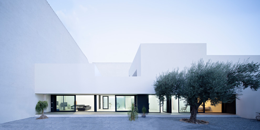 Modelo de fachada blanca actual grande de dos plantas con revestimiento de estuco y tejado plano