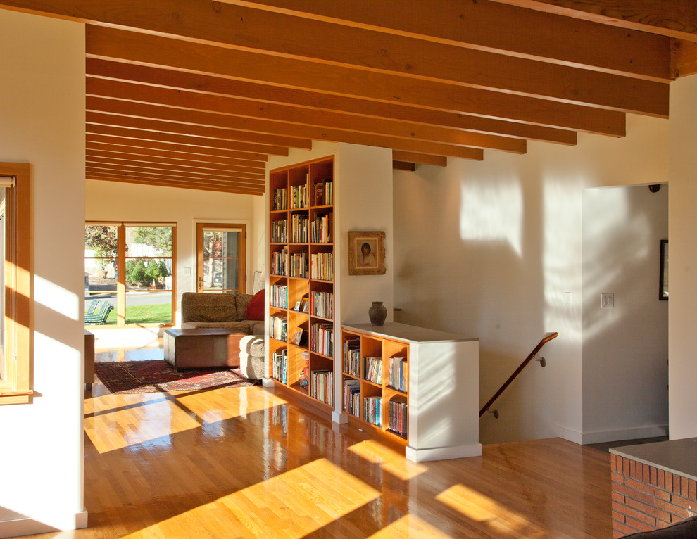 Пример оригинального дизайна: открытая гостиная комната среднего размера в стиле ретро с оранжевым полом, с книжными шкафами и полками, белыми стенами и темным паркетным полом без телевизора