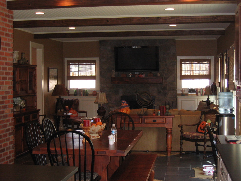 На фото: большая открытая гостиная комната в стиле кантри с коричневыми стенами, полом из сланца, стандартным камином, фасадом камина из камня и телевизором на стене с