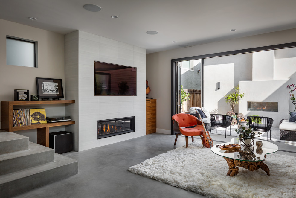 Ejemplo de sala de estar actual con paredes beige, suelo de cemento, chimenea lineal, marco de chimenea de baldosas y/o azulejos, suelo gris y alfombra