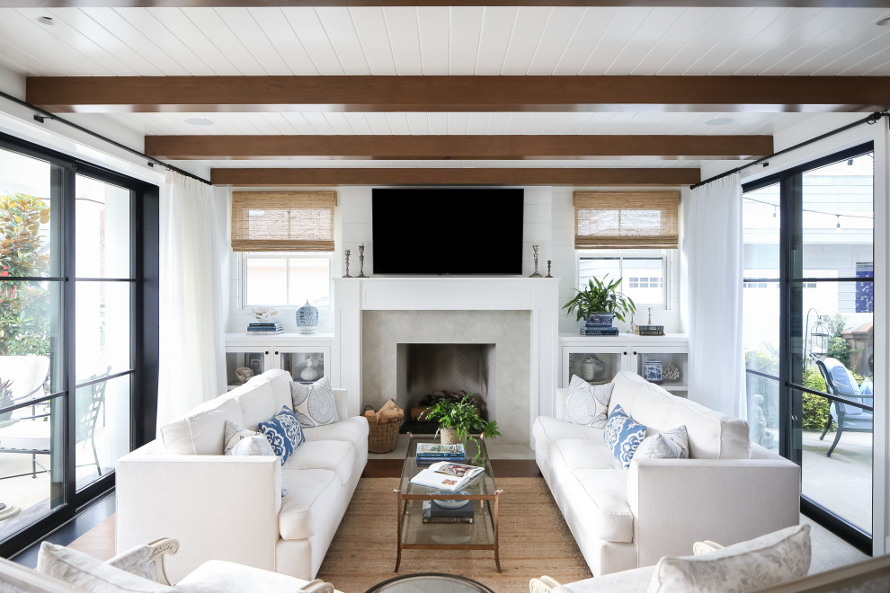 Maritimes Wohnzimmer mit weißer Wandfarbe, dunklem Holzboden, Kamin, Kaminumrandung aus Beton, TV-Wand und freigelegten Dachbalken in Orange County