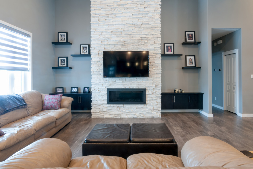 This is an example of a large contemporary open plan games room in Other with grey walls, dark hardwood flooring, a ribbon fireplace, a stone fireplace surround, a wall mounted tv and brown floors.