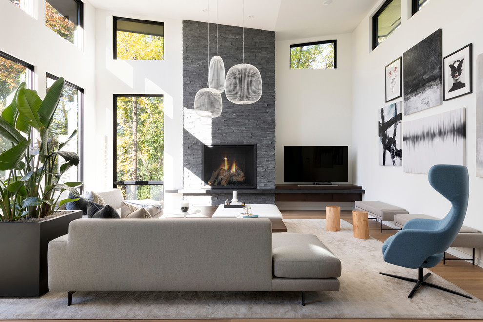 Modelo de sala de estar abierta contemporánea grande con paredes blancas, suelo de madera en tonos medios, todas las chimeneas, marco de chimenea de piedra, televisor independiente y suelo marrón