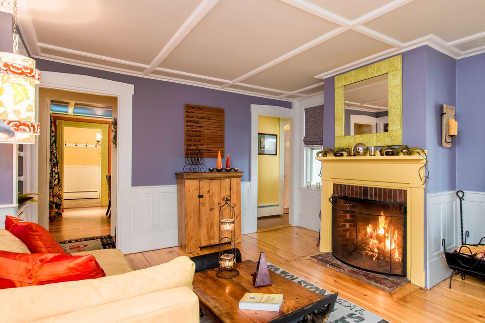 Imagen de sala de estar con biblioteca campestre de tamaño medio con paredes púrpuras, suelo de madera en tonos medios, todas las chimeneas y marco de chimenea de madera