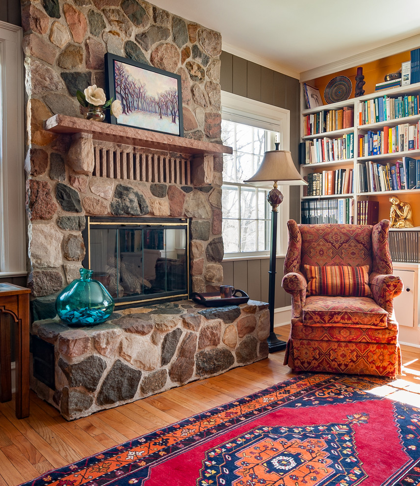 Imagen de sala de estar con biblioteca cerrada bohemia de tamaño medio con paredes beige, suelo de madera en tonos medios, todas las chimeneas y marco de chimenea de piedra
