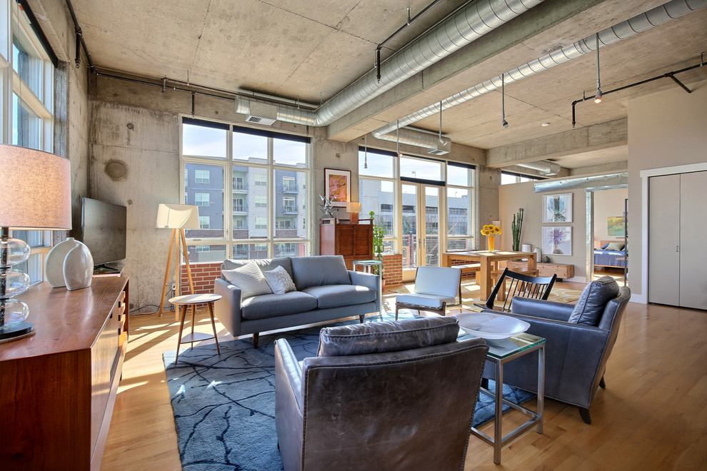 Offenes Industrial Wohnzimmer mit grauer Wandfarbe, braunem Holzboden und freistehendem TV in Denver