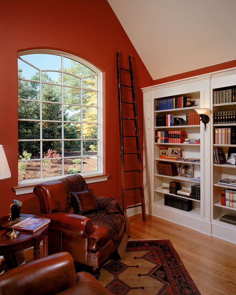 Esempio di un soggiorno chic con libreria, pareti rosse e pavimento in legno massello medio