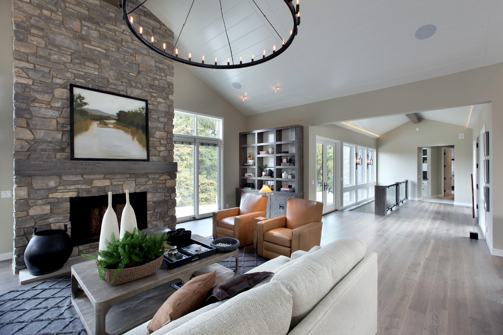 Foto de sala de estar abierta tradicional renovada grande con paredes beige, suelo de madera en tonos medios, chimenea de doble cara y marco de chimenea de piedra