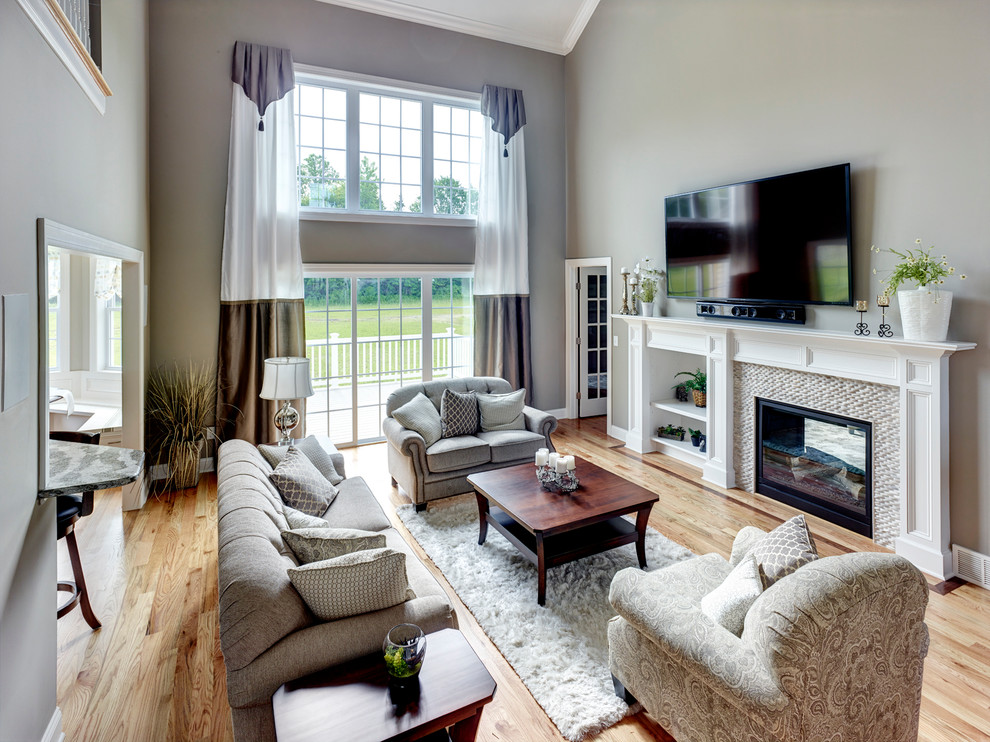 Ejemplo de sala de estar abierta tradicional renovada con paredes grises, suelo de madera en tonos medios, chimenea de doble cara, marco de chimenea de piedra y televisor colgado en la pared