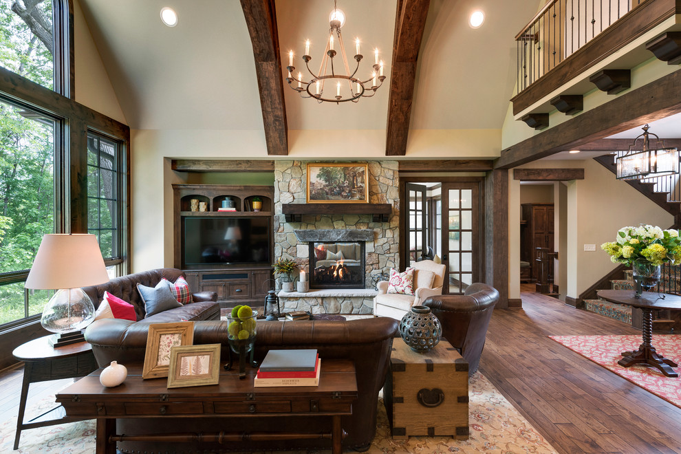 Huge mountain style open concept medium tone wood floor family room photo in Minneapolis with beige walls, a two-sided fireplace, a stone fireplace and a wall-mounted tv