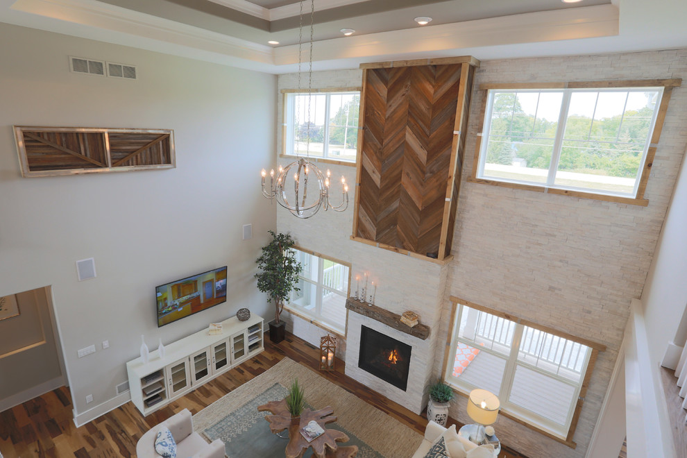 This is an example of an expansive classic open plan games room in Milwaukee with grey walls, light hardwood flooring, a standard fireplace, a stone fireplace surround and a wall mounted tv.