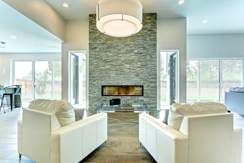 Foto de sala de estar abierta actual de tamaño medio con paredes blancas, suelo de madera clara, chimenea lineal, marco de chimenea de piedra y pared multimedia