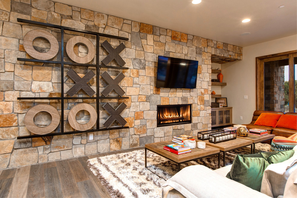 Ejemplo de sala de estar rústica con suelo de madera en tonos medios, chimenea lineal, marco de chimenea de piedra, televisor colgado en la pared y alfombra