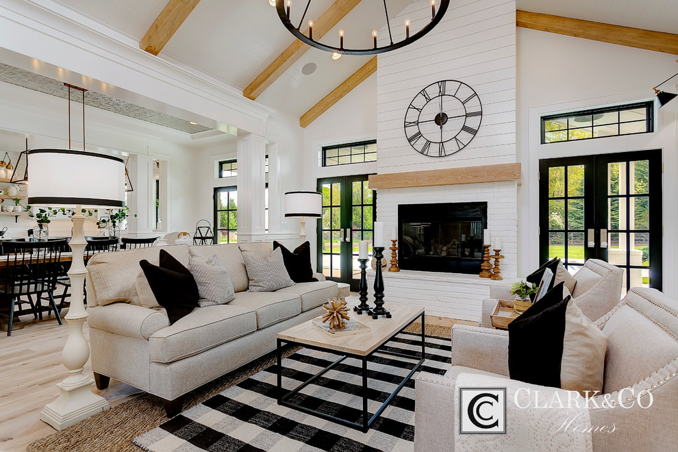 Modelo de sala de estar de estilo de casa de campo grande con paredes blancas, suelo de madera clara, todas las chimeneas y pared multimedia