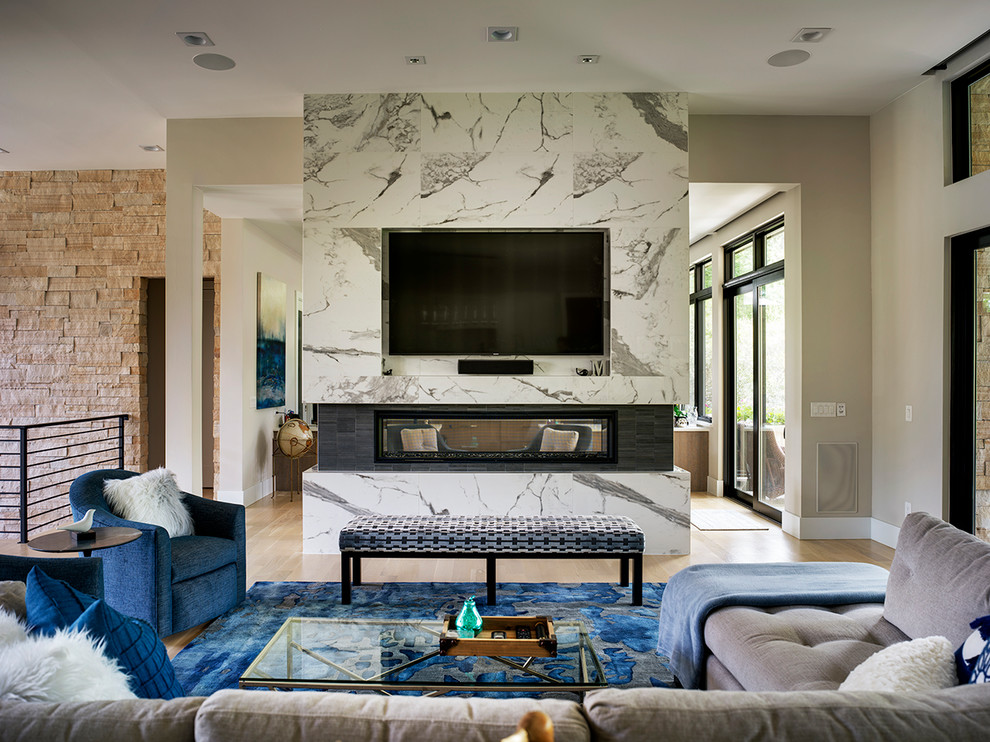 Ejemplo de sala de estar contemporánea con paredes beige, suelo de madera clara, chimenea de doble cara y pared multimedia