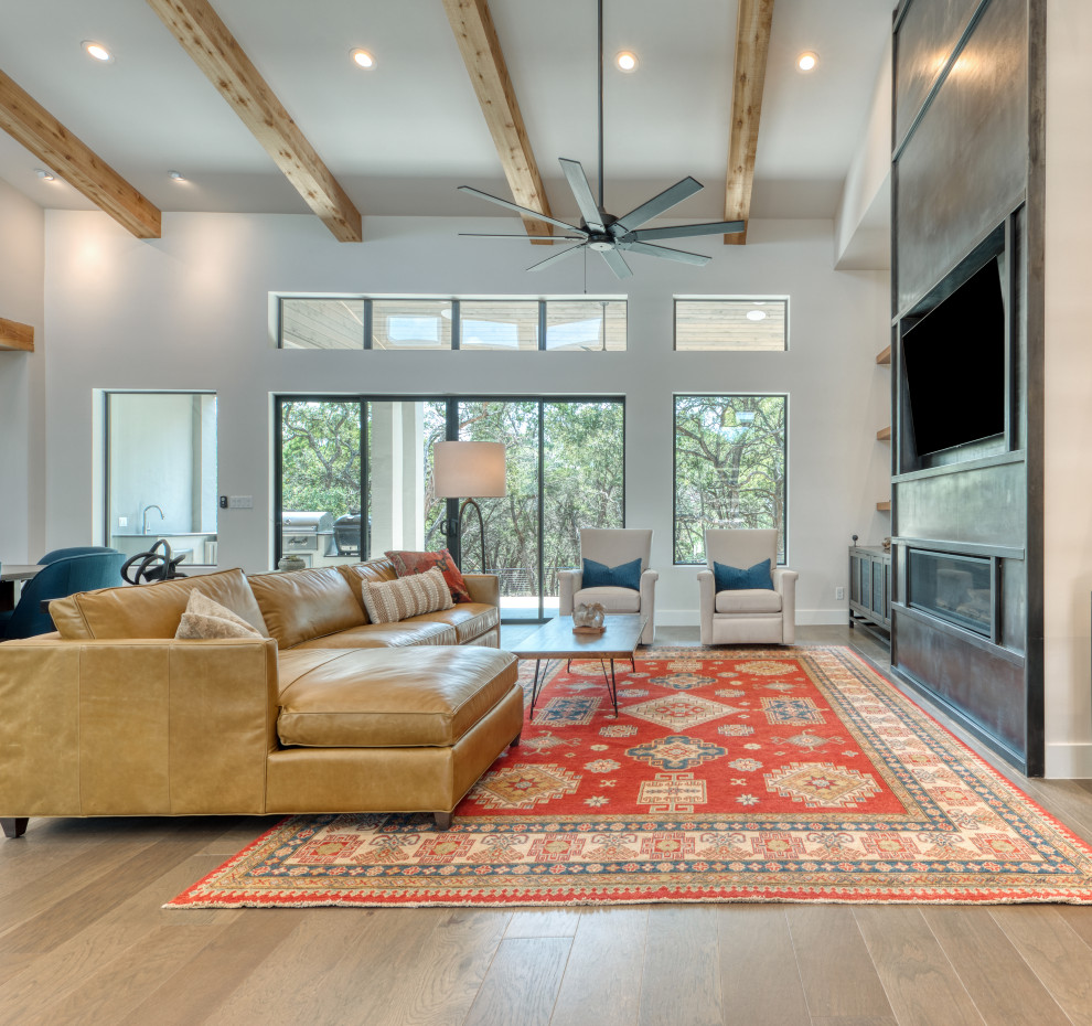 Photo of a large industrial open plan games room in Austin with grey walls, light hardwood flooring, a ribbon fireplace, a metal fireplace surround, a built-in media unit and brown floors.