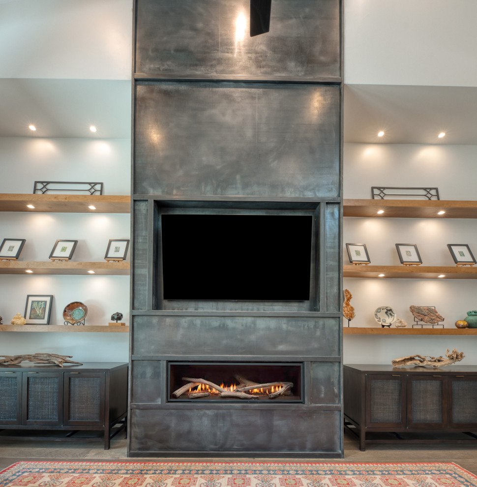 This is an example of a large industrial open plan games room in Austin with grey walls, light hardwood flooring, a ribbon fireplace, a metal fireplace surround, a built-in media unit and brown floors.