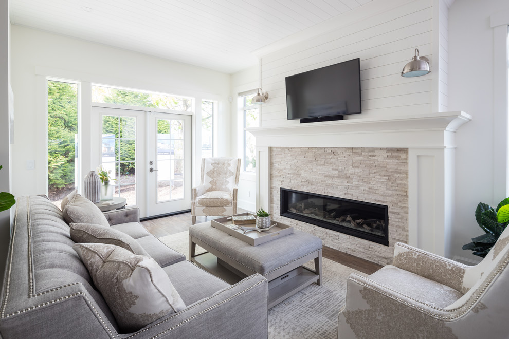 Landhaus Wohnzimmer mit weißer Wandfarbe, braunem Holzboden, Gaskamin, Kaminumrandung aus Stein, TV-Wand und braunem Boden in Vancouver
