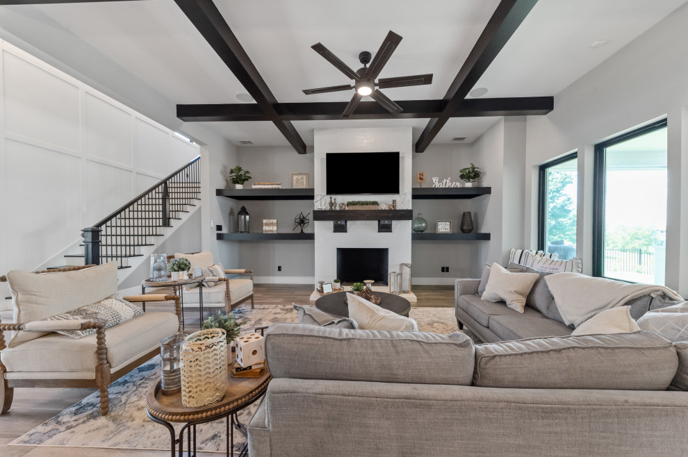 Inspiration for a large country open concept medium tone wood floor, brown floor and exposed beam family room remodel in Dallas with gray walls, a wood stove, a brick fireplace and a wall-mounted tv