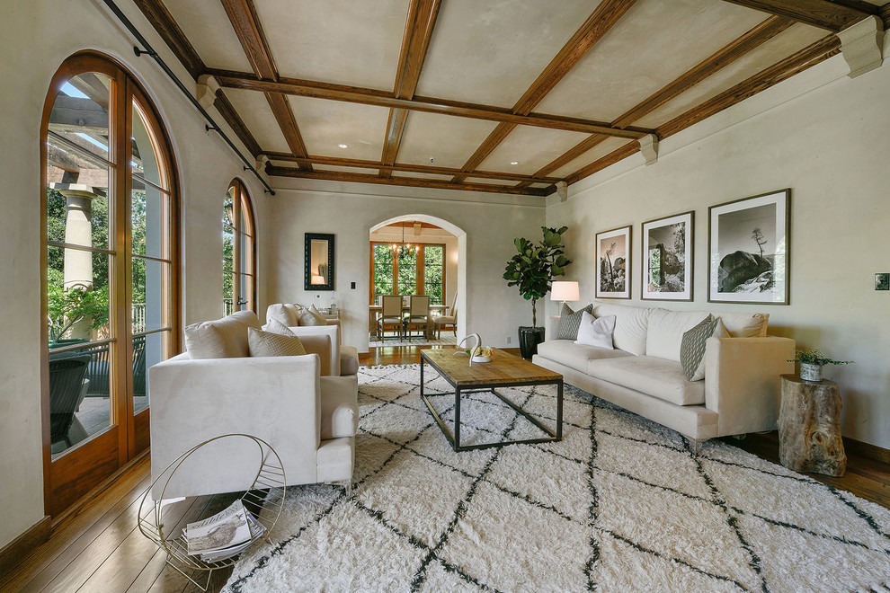 Diseño de sala de estar mediterránea con paredes blancas, suelo de madera en tonos medios, todas las chimeneas, marco de chimenea de piedra, televisor colgado en la pared y suelo marrón